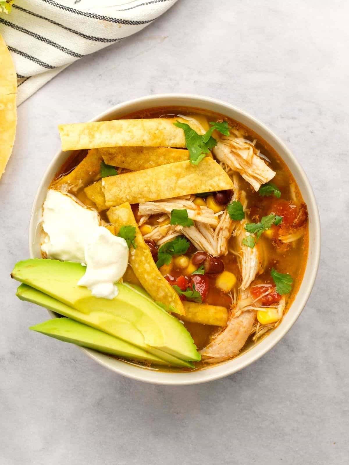 Bowl of Instant Pot Chicken Tortilla Soup topped with avocado, lime, and tortilla strips. 