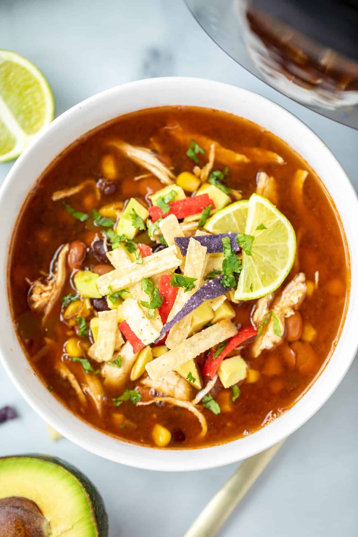 Bowl of Instant Pot Chicken Tortilla Soup topped with avocado, lime, and tortilla strips.