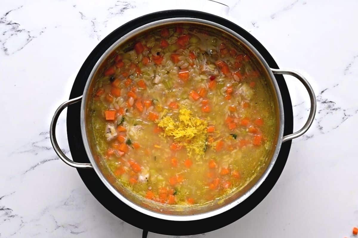 Stock pot with orzo soup with lemon zest on top of soup.