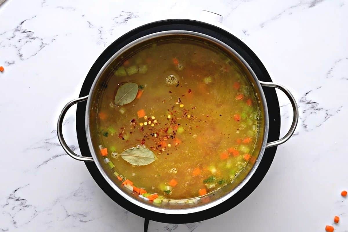 Stock pot with broth and veggies for chicken orzo soup.