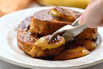 Fork and knife sicing into french toast with banana rum sauce.