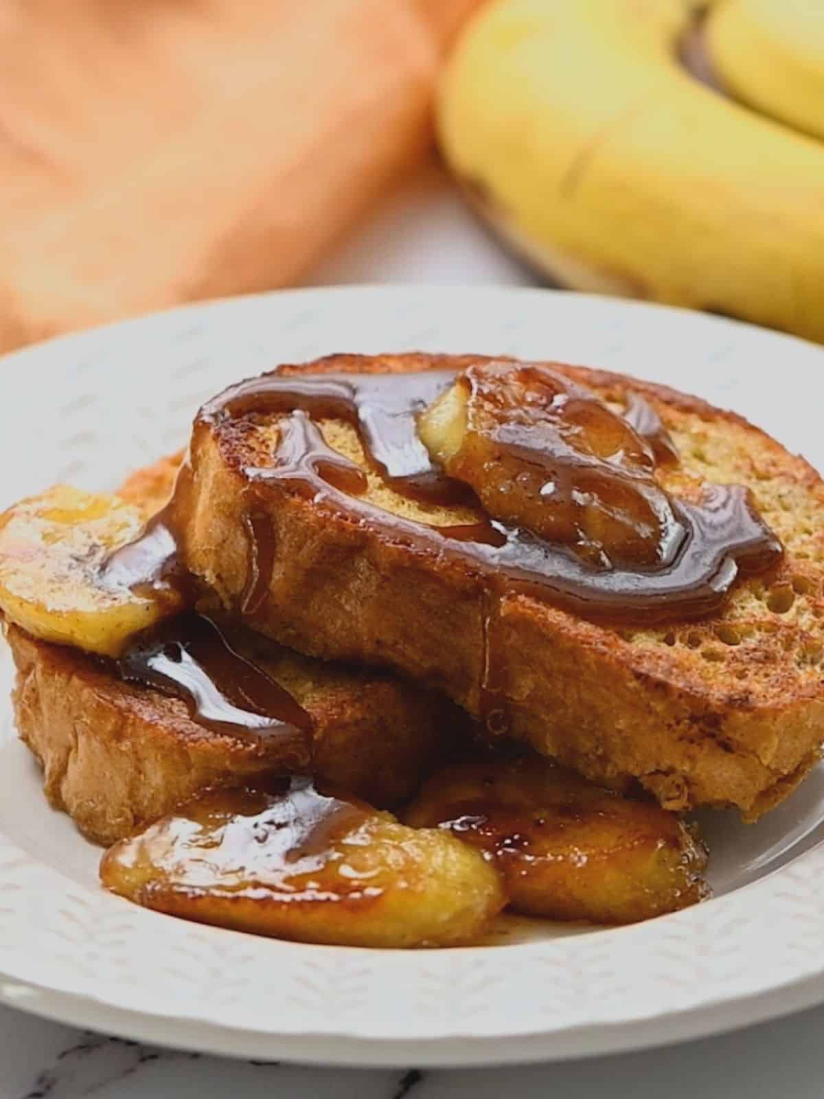French toast on white plate with bananas fosters sauce.
