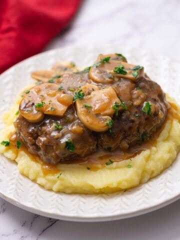 Chopped Steak with mushroom gravy served over mashed potatoes on white plate.