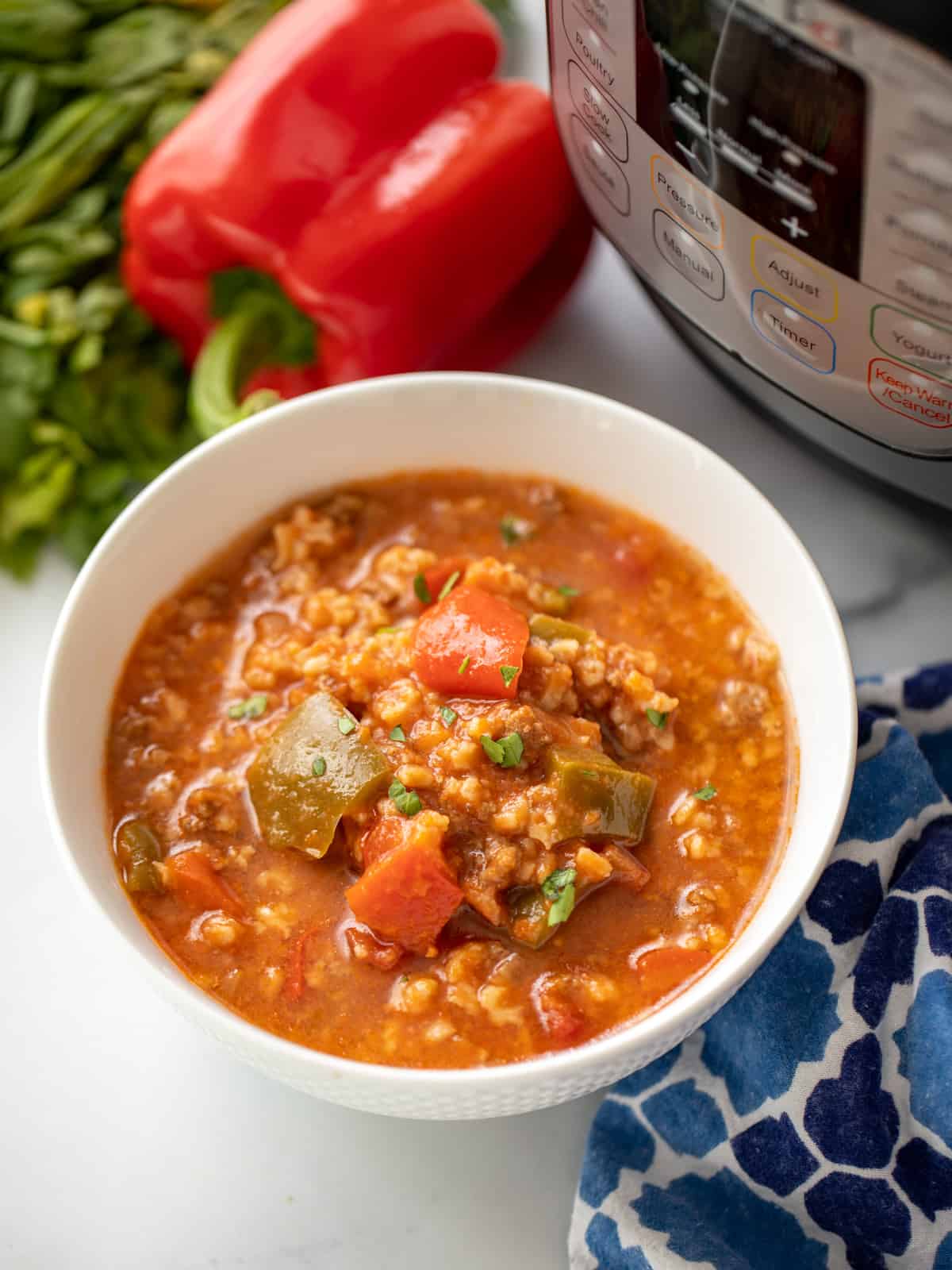 Bowl of Instant Pot Stuffed Pepper Soup next to instant pot and fresh peppers. 