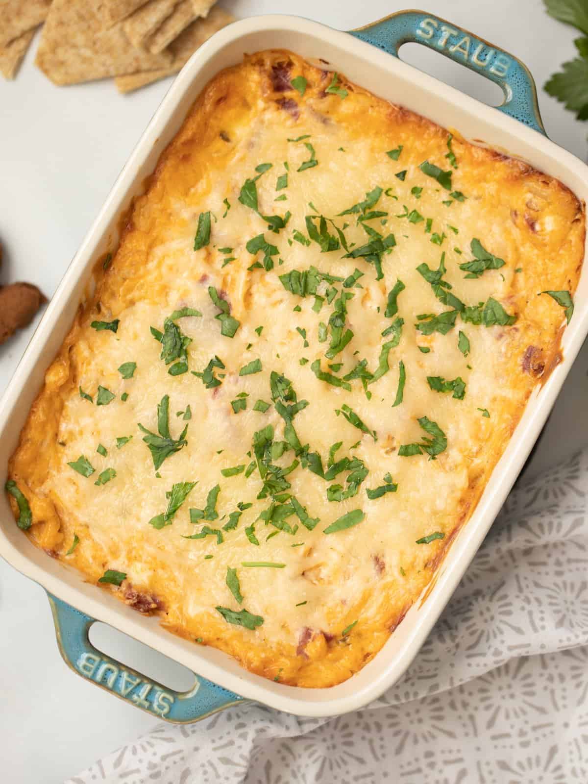 Hot Reuben dip in blue casserole dish topped with fresh parsley.