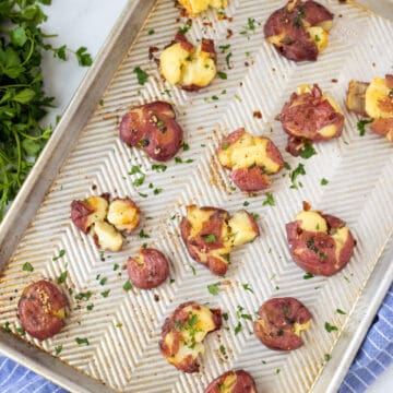 Smashed Potatoes on sheet pan brushed with garlic butter and topped with fresh parsley.