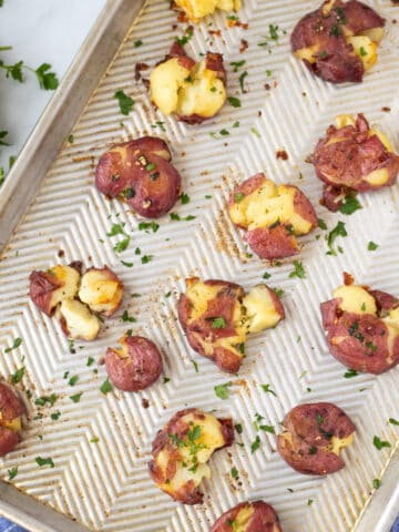 Smashed Potatoes on sheet pan brushed with garlic butter and topped with fresh parsley.