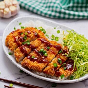 Sliced Chicken Katsu on plate served with rice and shredded cabbage.