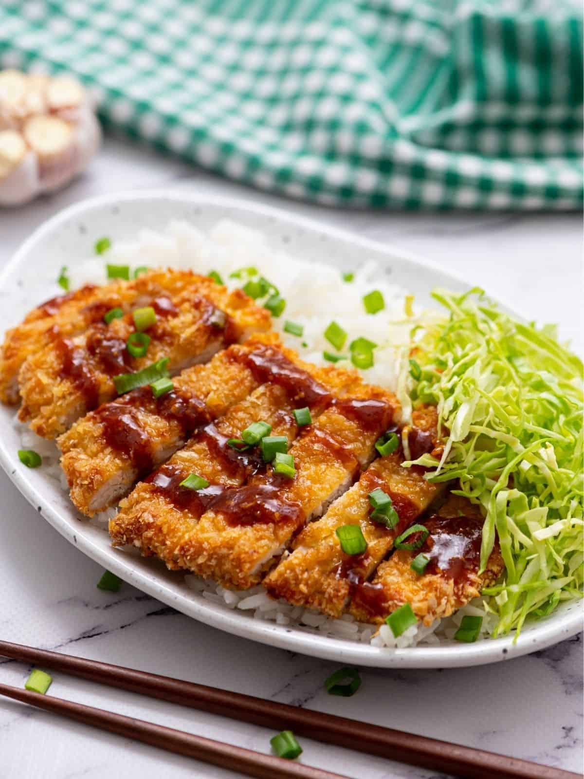 Sliced Chicken Katsu on plate served with rice and shredded cabbage.