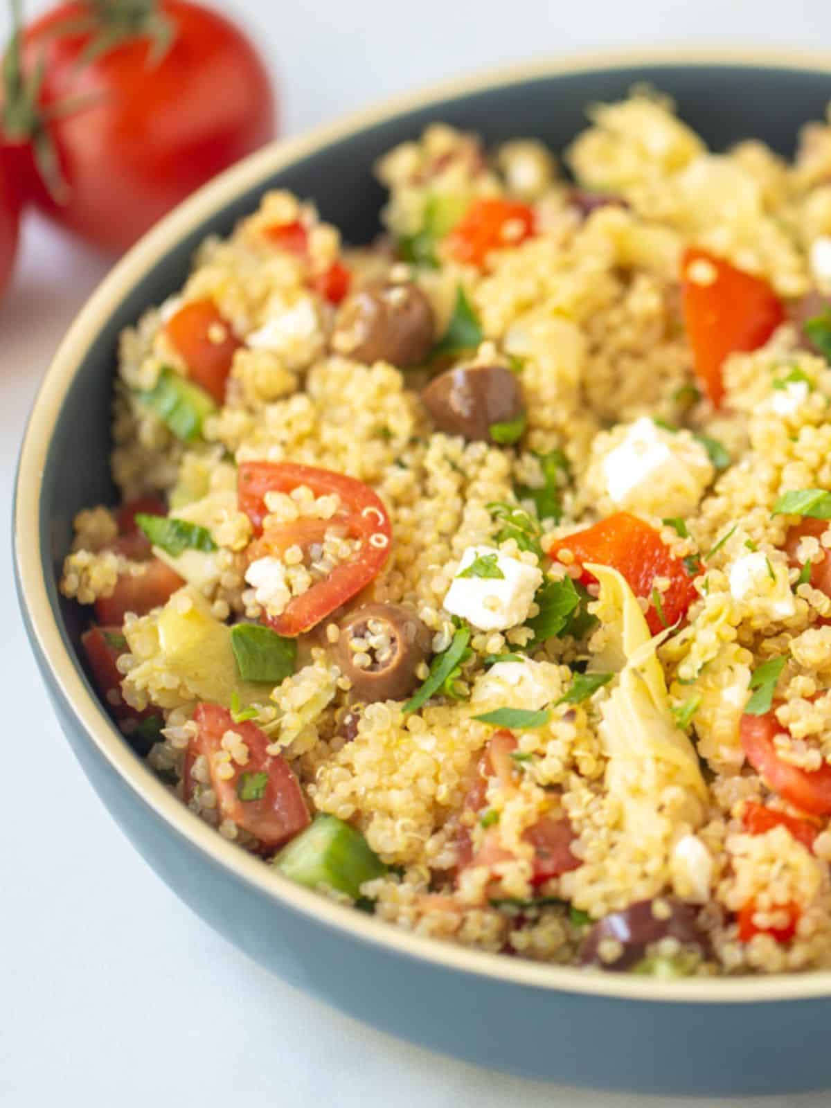 Bowl of Greek Quinoa Salad with parsley with tomatoes in the background.