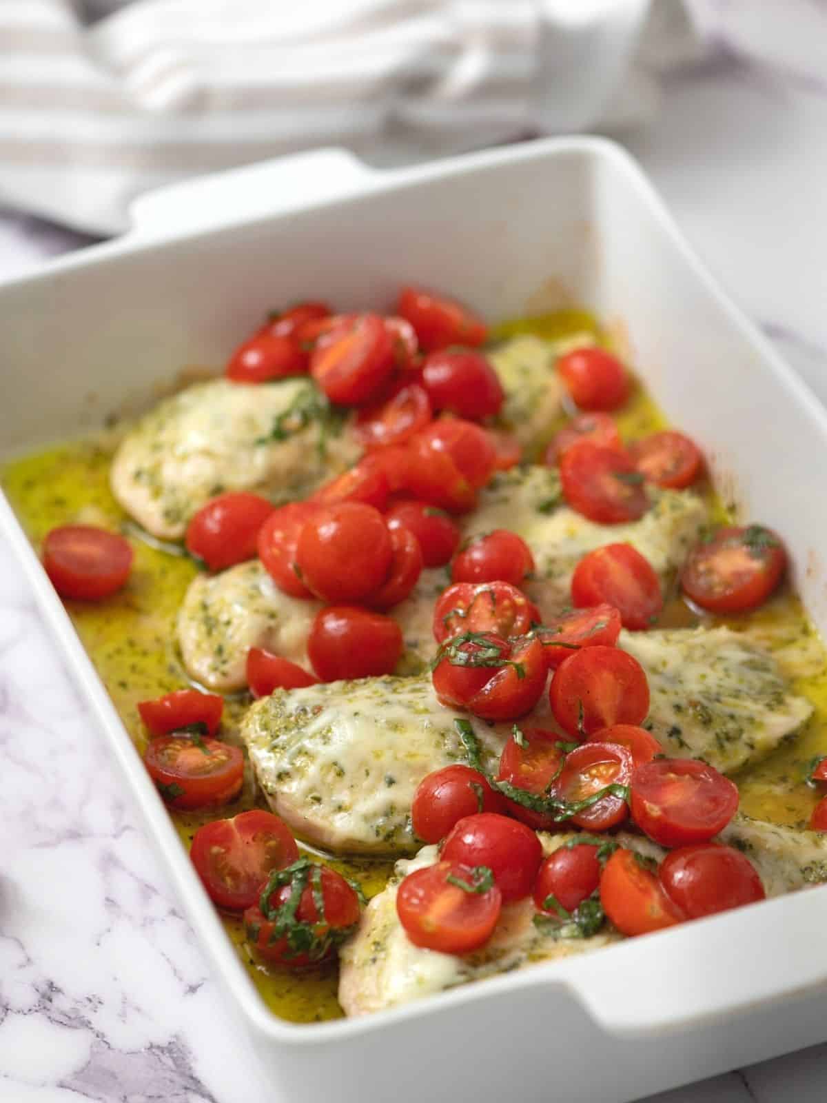 Baked Chicken topped with pesto, cheese, and fresh tomatoes.