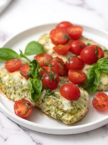 Chicken breasts with pesto, mozzarella and tomatoes on white plate.