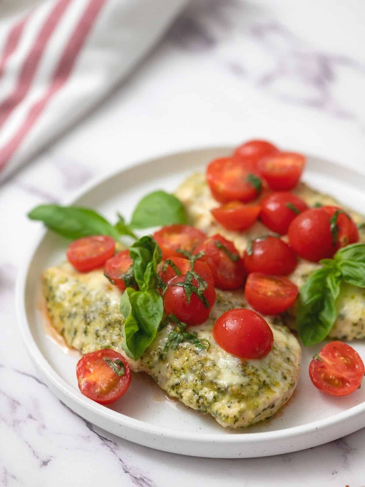 Plate with baked pesto chicken topped with fresh tomatoes and basil.