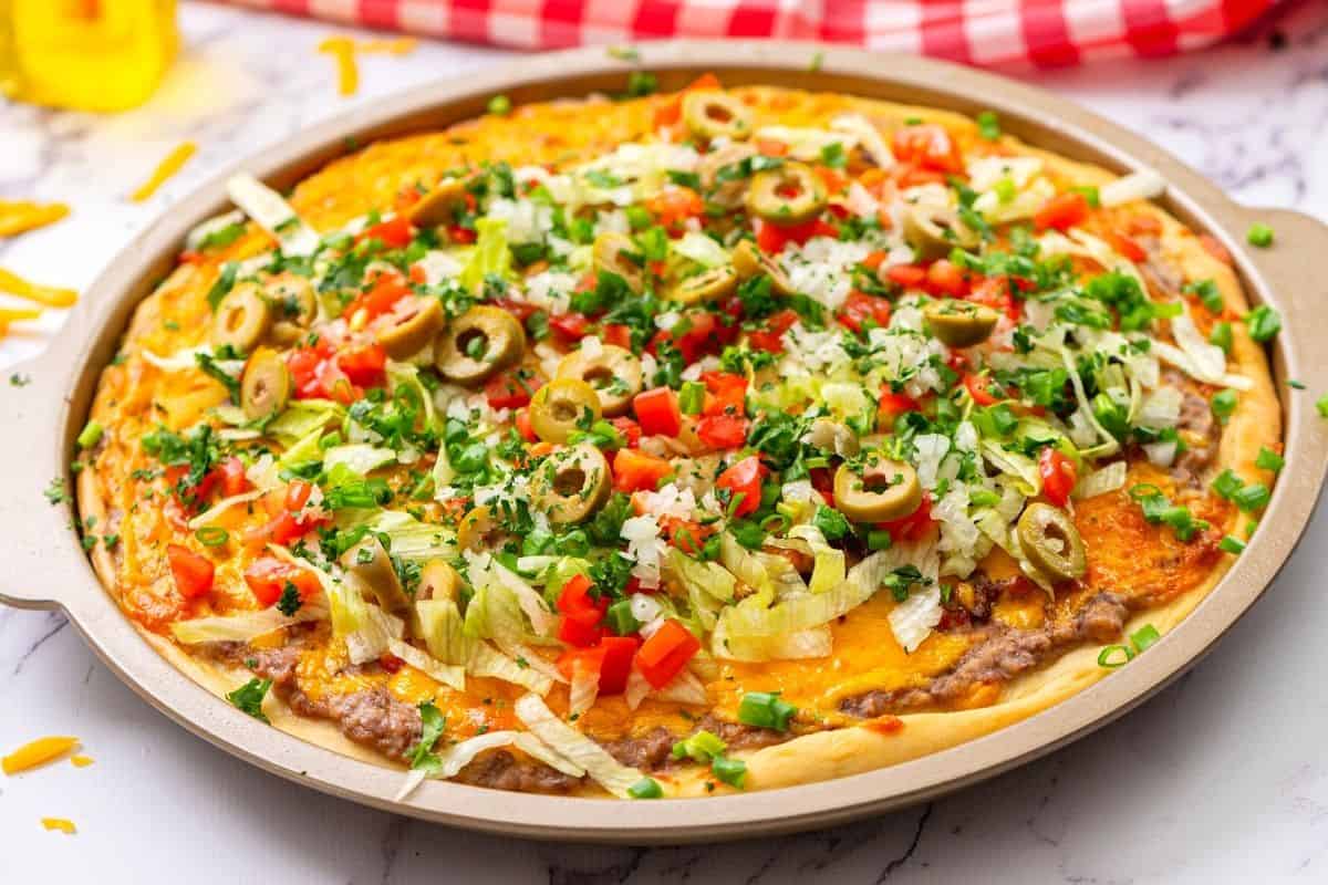 Taco Pizza topped with lettuce, cilantro, tomatoes, and olives.