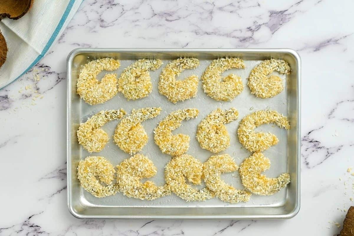 Shrimp breaded in coconut and breadcrumbs on sheet pan.