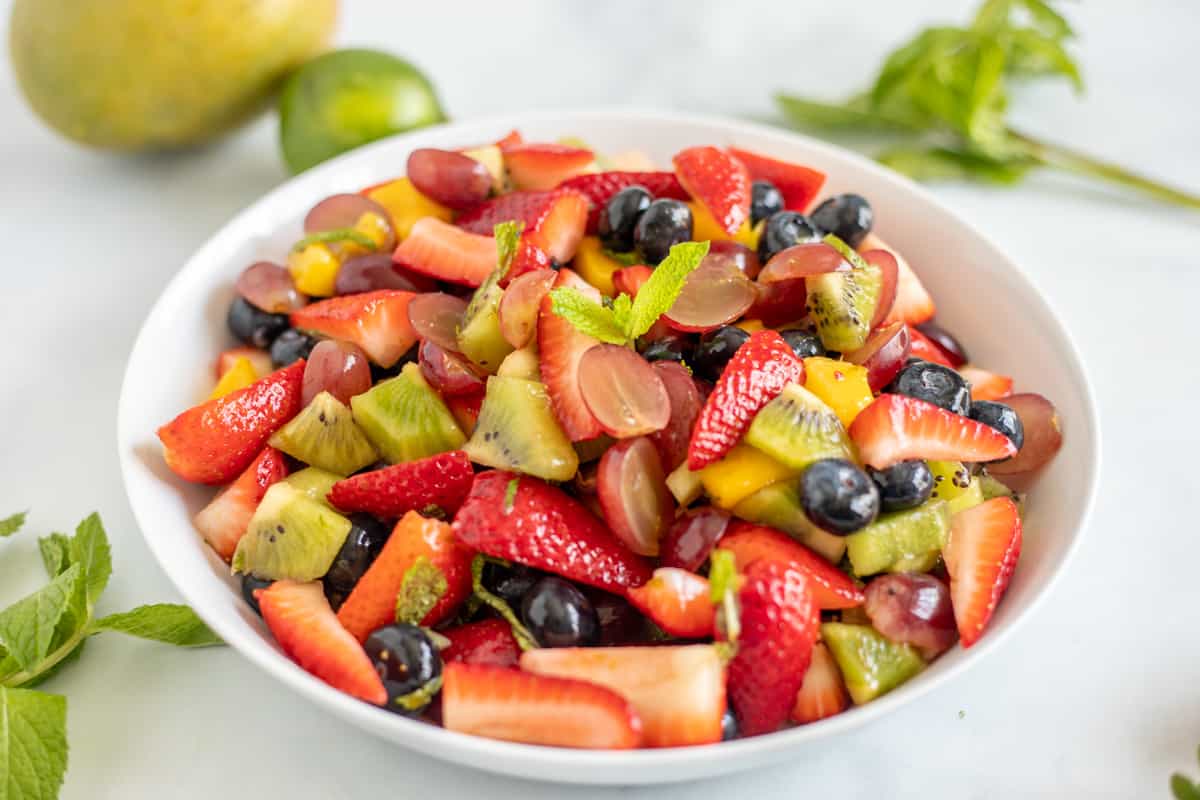 Fruit Salad in white serving dish topped with fresh mint.