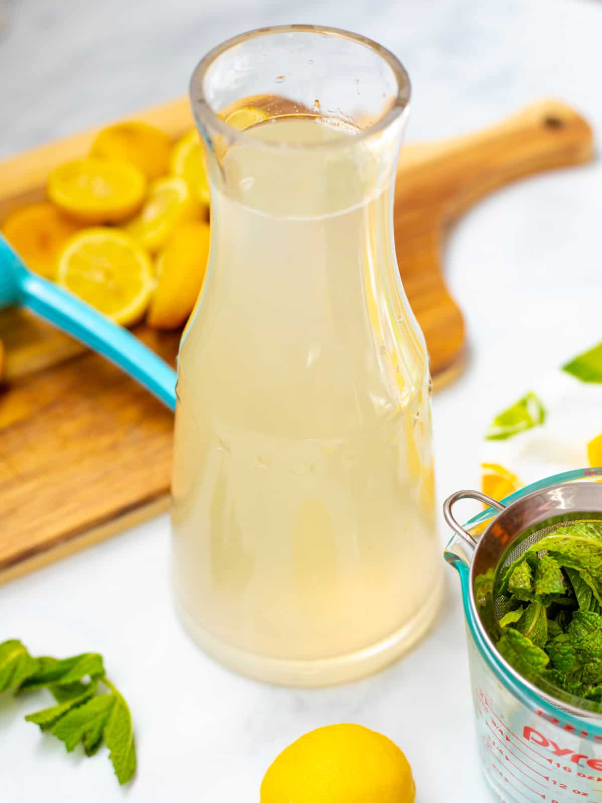 Clear pitcher of mint lemonade next to fresh mint and lemons.