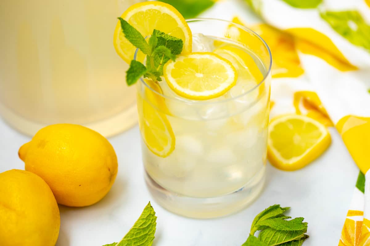 Class of mint lemonad with sliced lemon and fresh mint next to fresh lemons.