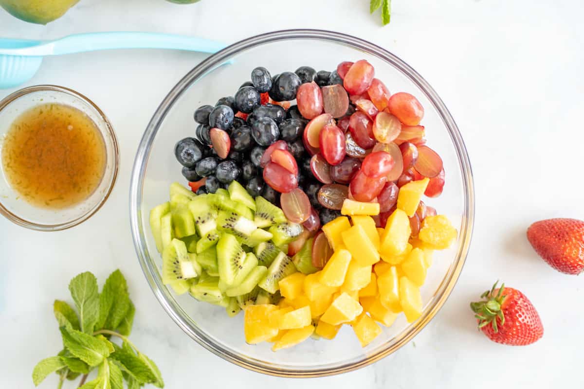 Kiwi, mango, grapes, blueberries, and strawberries in mixing bowl.