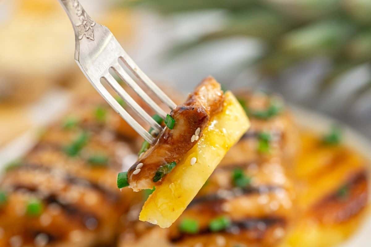 Fork holding bite of chicken and pineapple.
