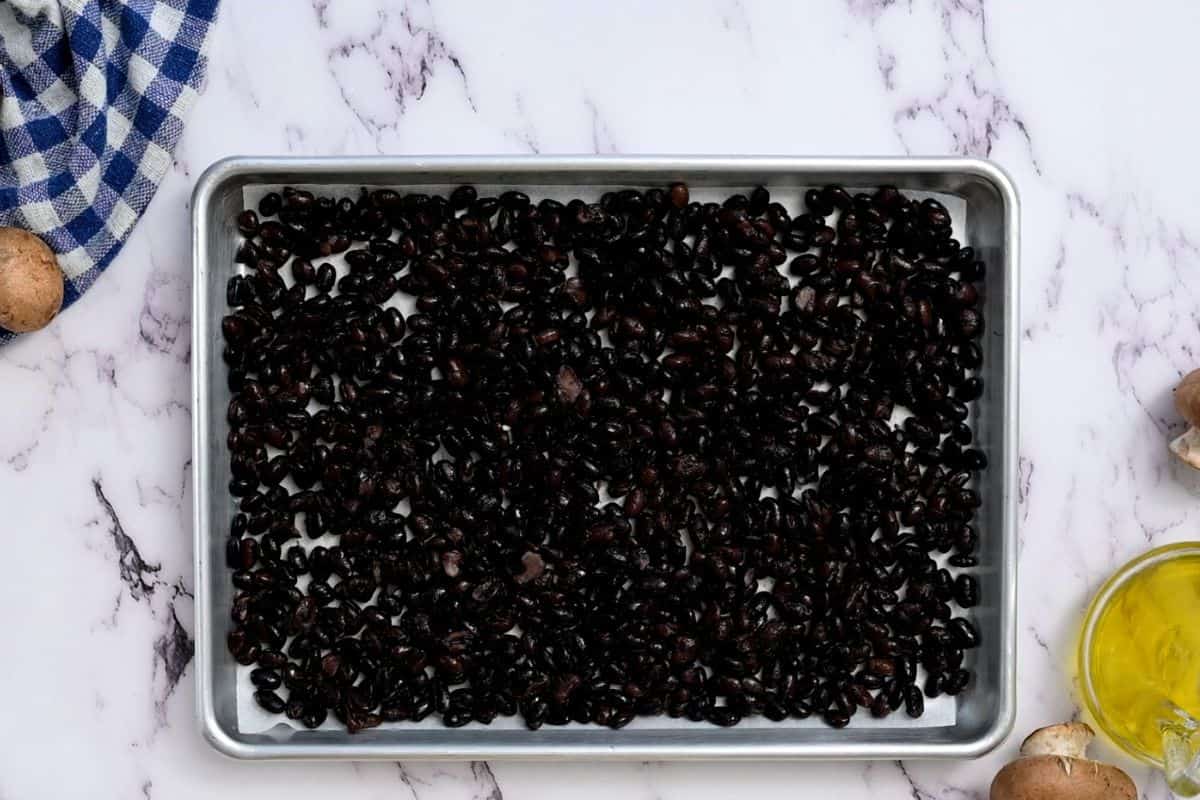 Black beans spread out on a sheet pan with parchment paper. 