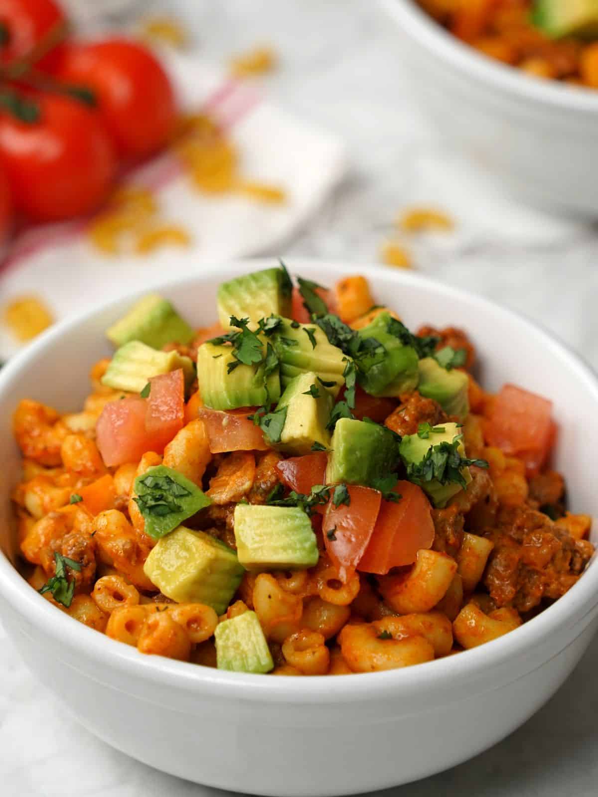 Bowl of taco pasta topped with diced avocado, tomato, and cheese.