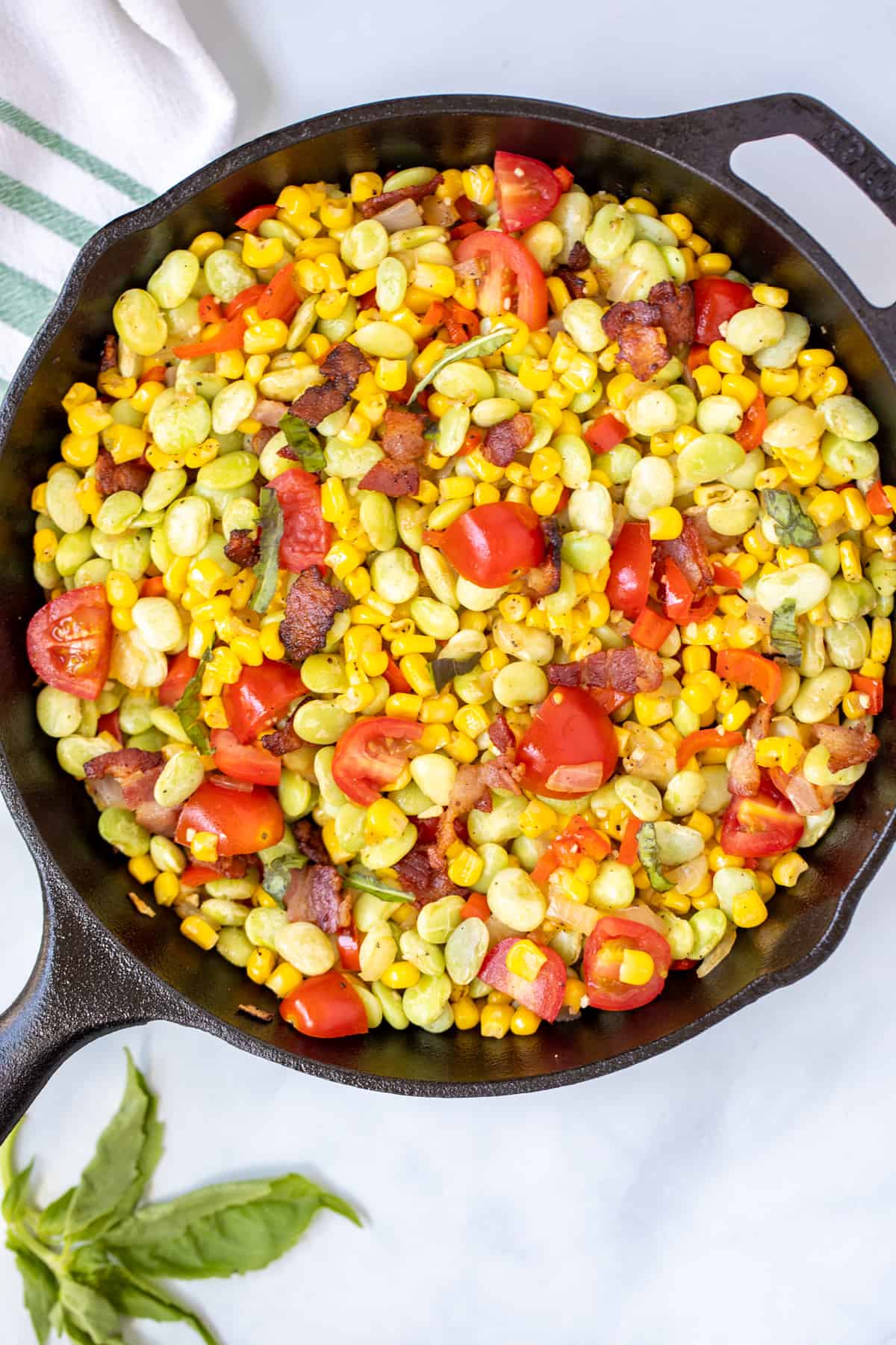 Cast Iron Skillet with Succotash topped with cherry tomatoes and basil.