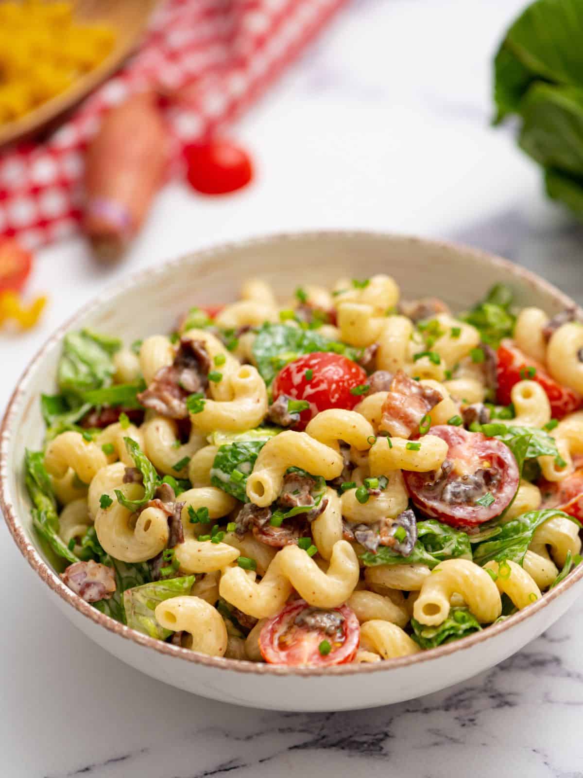 Bowl of creamy BLT Pasta Salad with grape tomatoes in background.