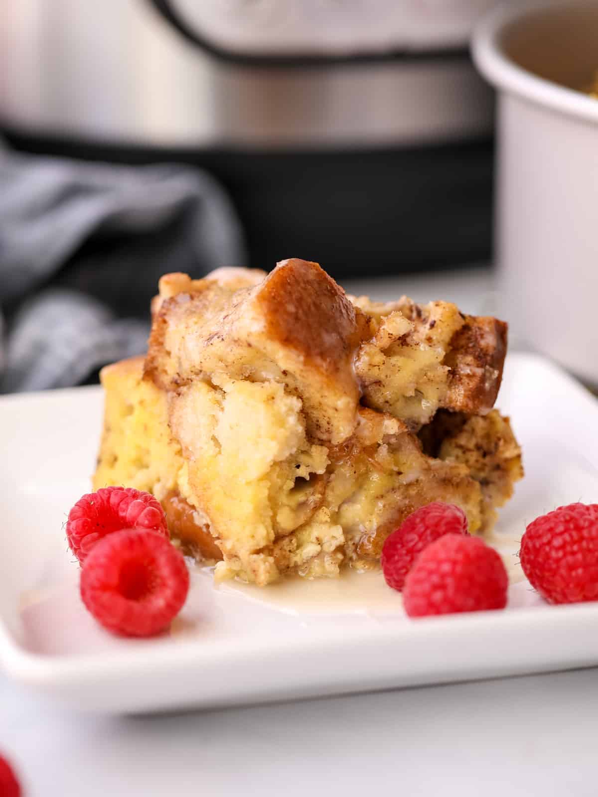 Slice of Instant Pot French Toast Casserole on white plate with raspberries.