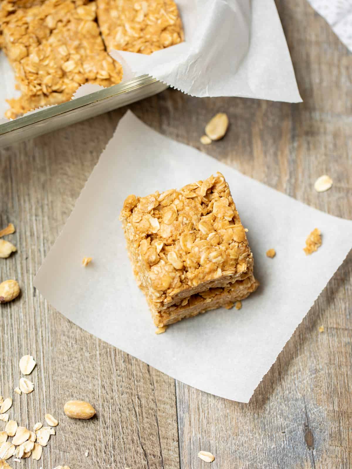 PB Oat Bars stack together on parchment paper next to tray of peanut butter oatmeal bars.