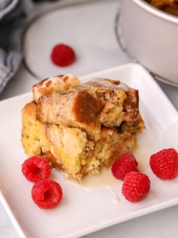 Slice of Instant Pot French Toast Casserole on white plate with raspberries.