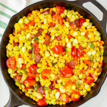 Cast Iron Skillet with Succotash topped with cherry tomatoes and basil.