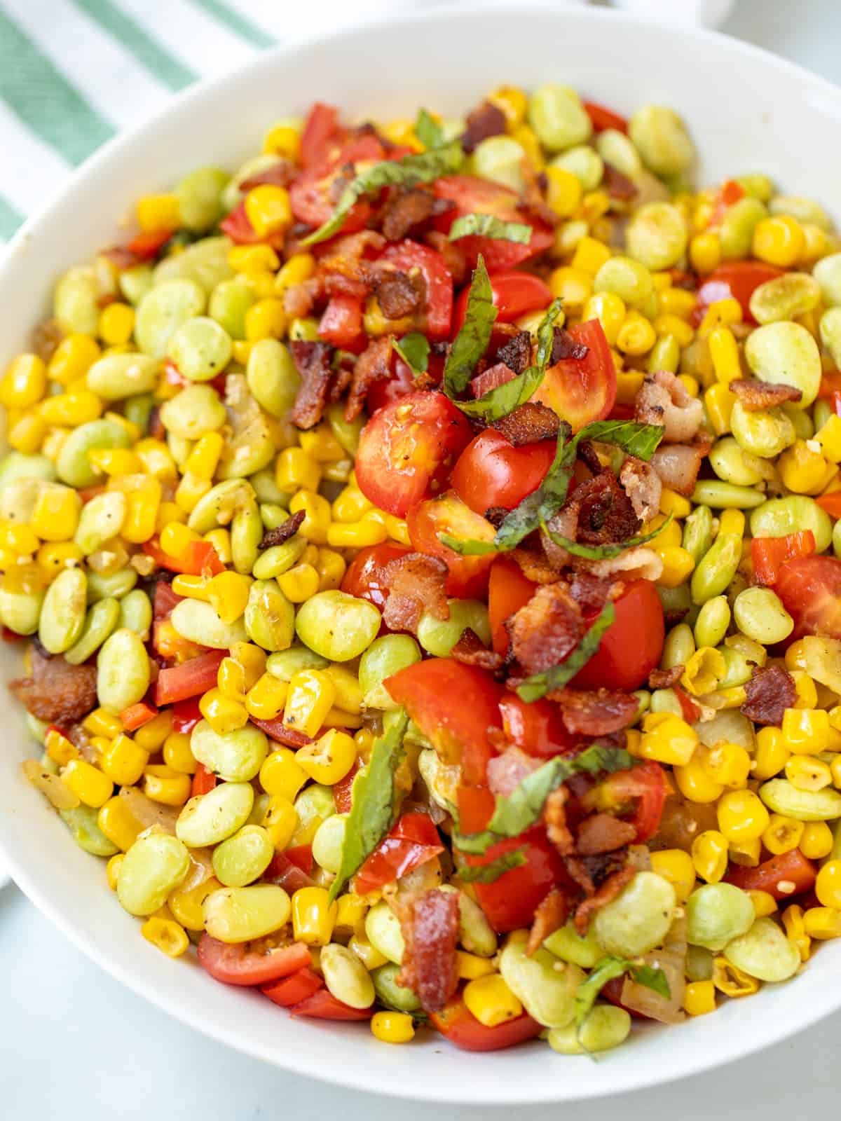 Succotash dished up in white dish with bacon and tomatoes.