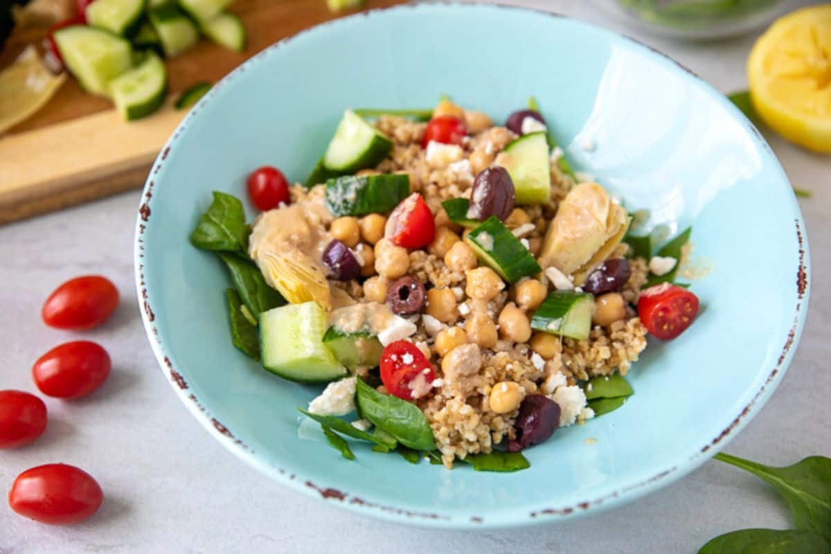 Quinoa salad with tomatoes, olives, cucumbers and feta in blue bowl.