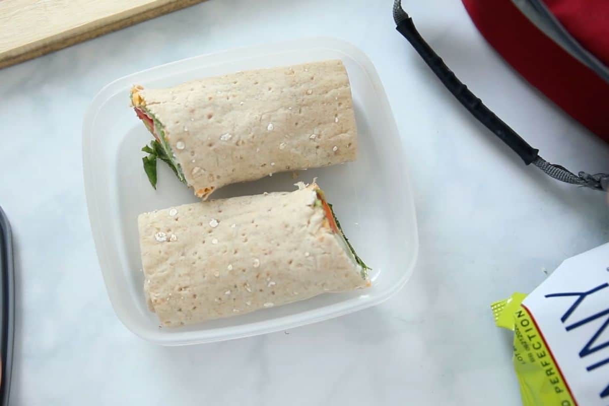 Veggie Wrap in lunch container next to lunchbox and bag of popcorn.