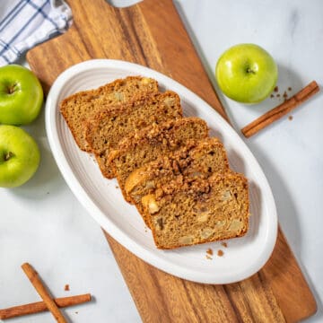 Sliced whole wheat apple bread with streusel on white plate with granny smith apples in background.