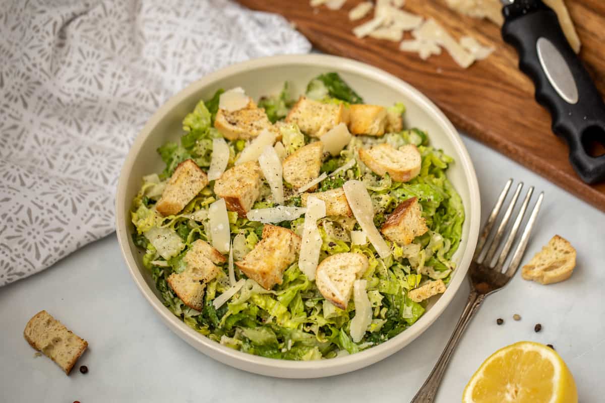 Caesar salad in serving dish with homemade croutons and fresh parmesan on side.