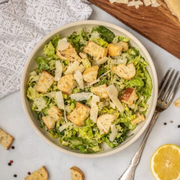 Caesar Salad with homemade croutons and parmesan next to fresh lemon and fork.