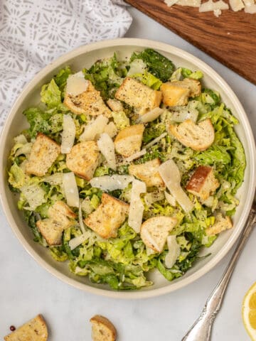 Caesar Salad with homemade croutons and parmesan next to fresh lemon and fork.