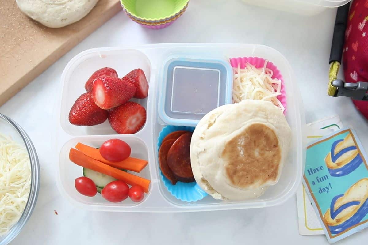 Pizza Lunchable with pepperoni, cheese, strawberries and veggies next to cute lunch note next to lunchbox.