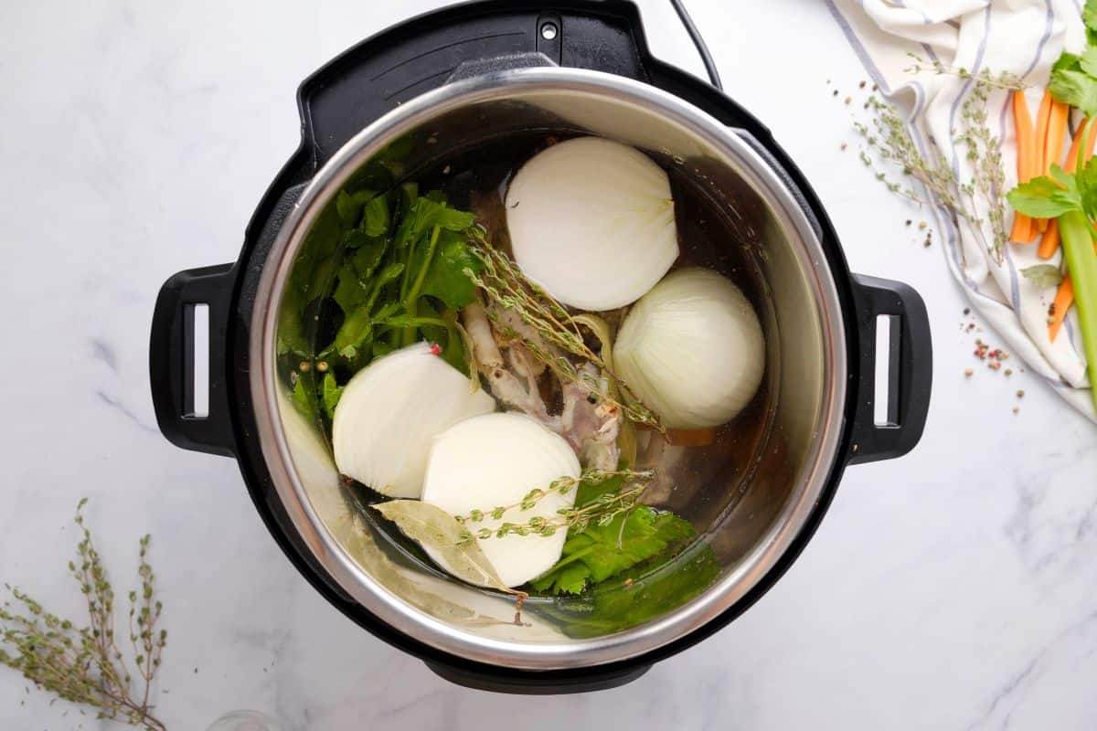 Chicken bones, vegetables, herbs and water in the inner pot in the instant pot.