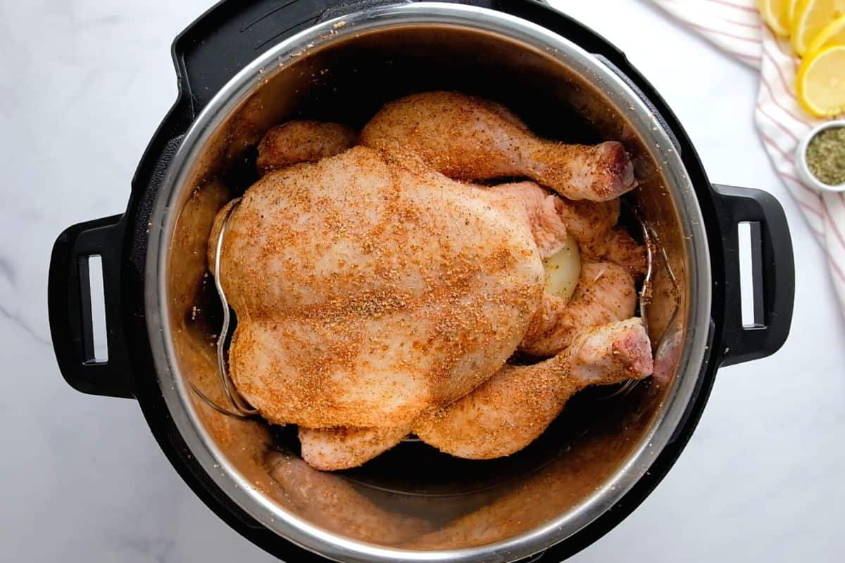 Seasoned whole chicken on trivet inside inner pot.