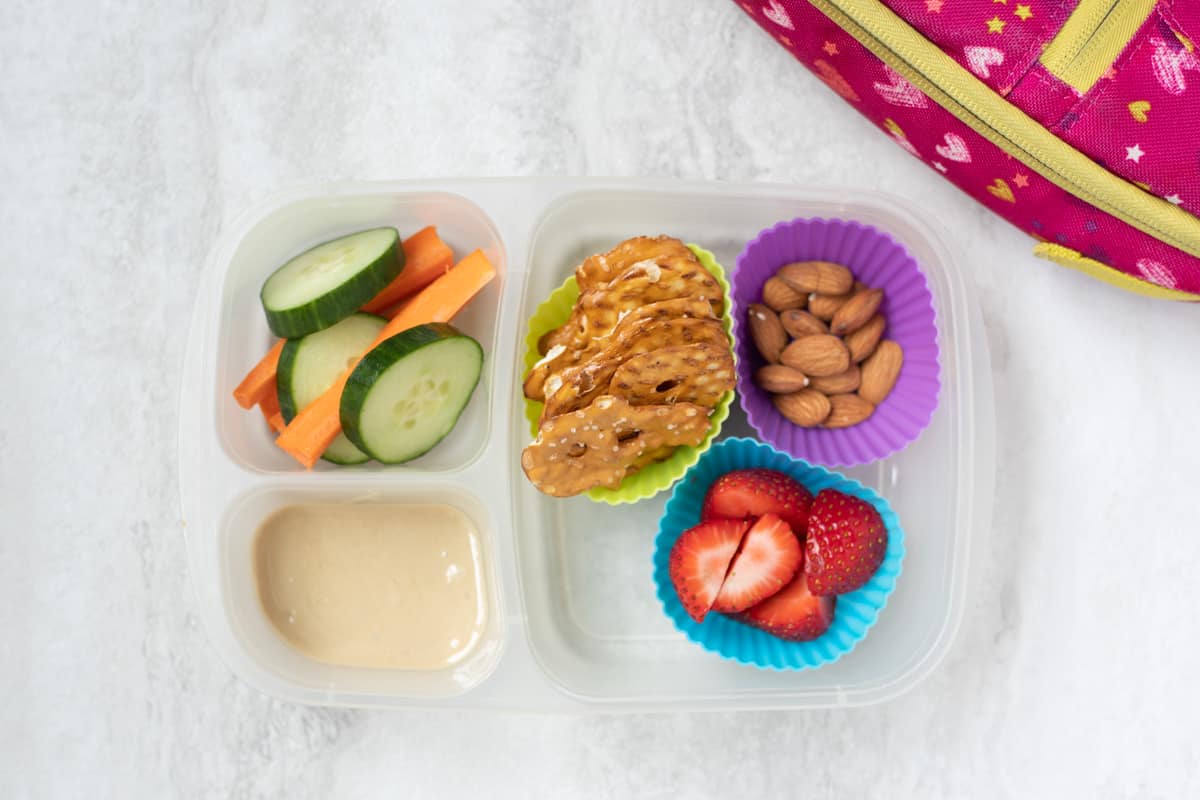 Lunch Container with hummus pretzels, veggies, fruit, and almonds.