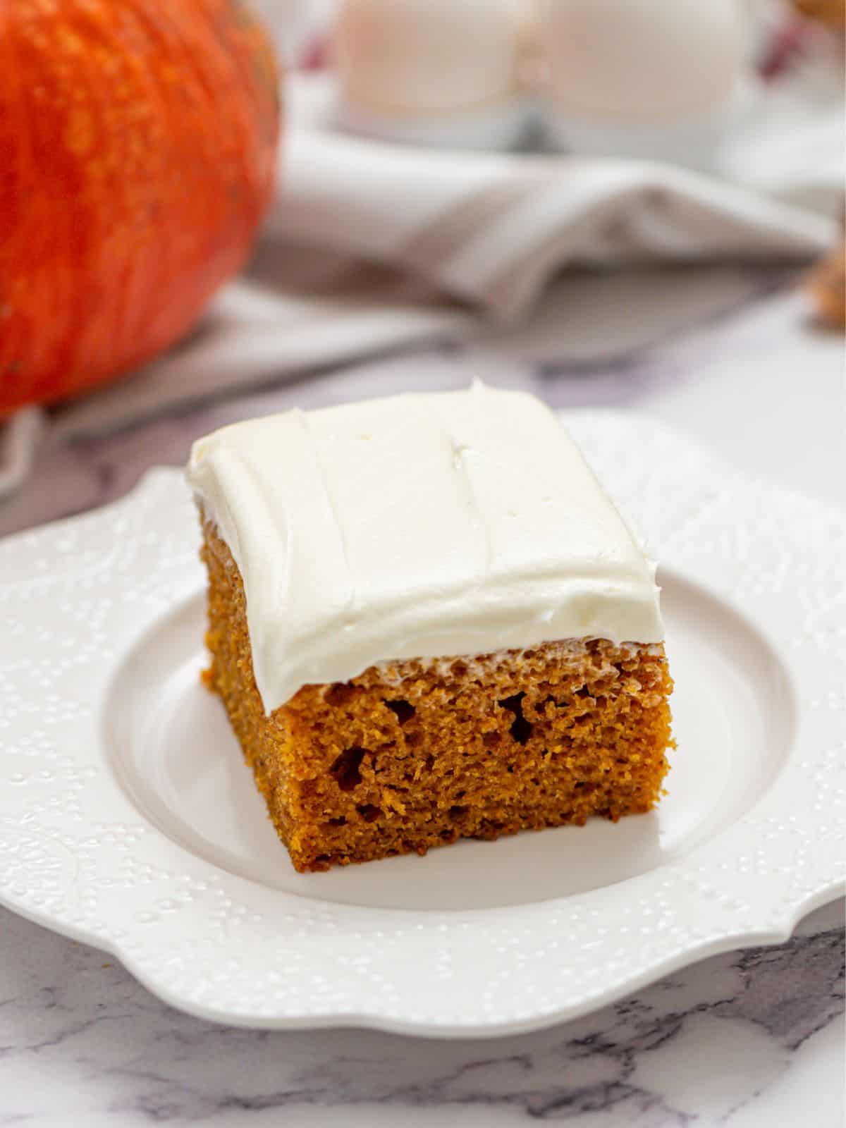 Slice of pumpkin cake with cream cheese frosting on white plate.