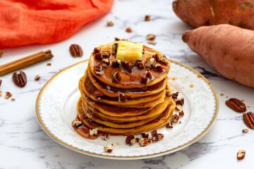Stack of pancakes on plate topped with maple syrup and chopped nuts.