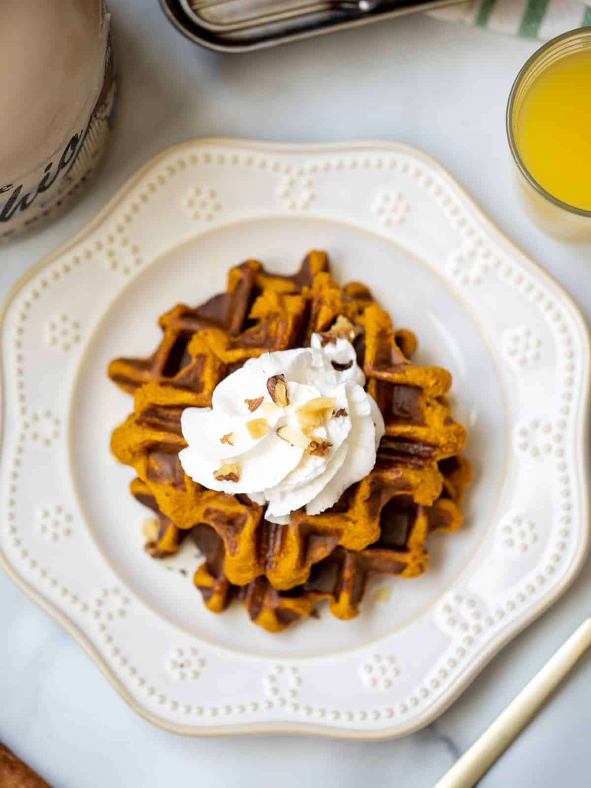 Top view of Sweet Potato Waffles on cream plate topped with whipped cream, maple syrup, and chopped walnuts.