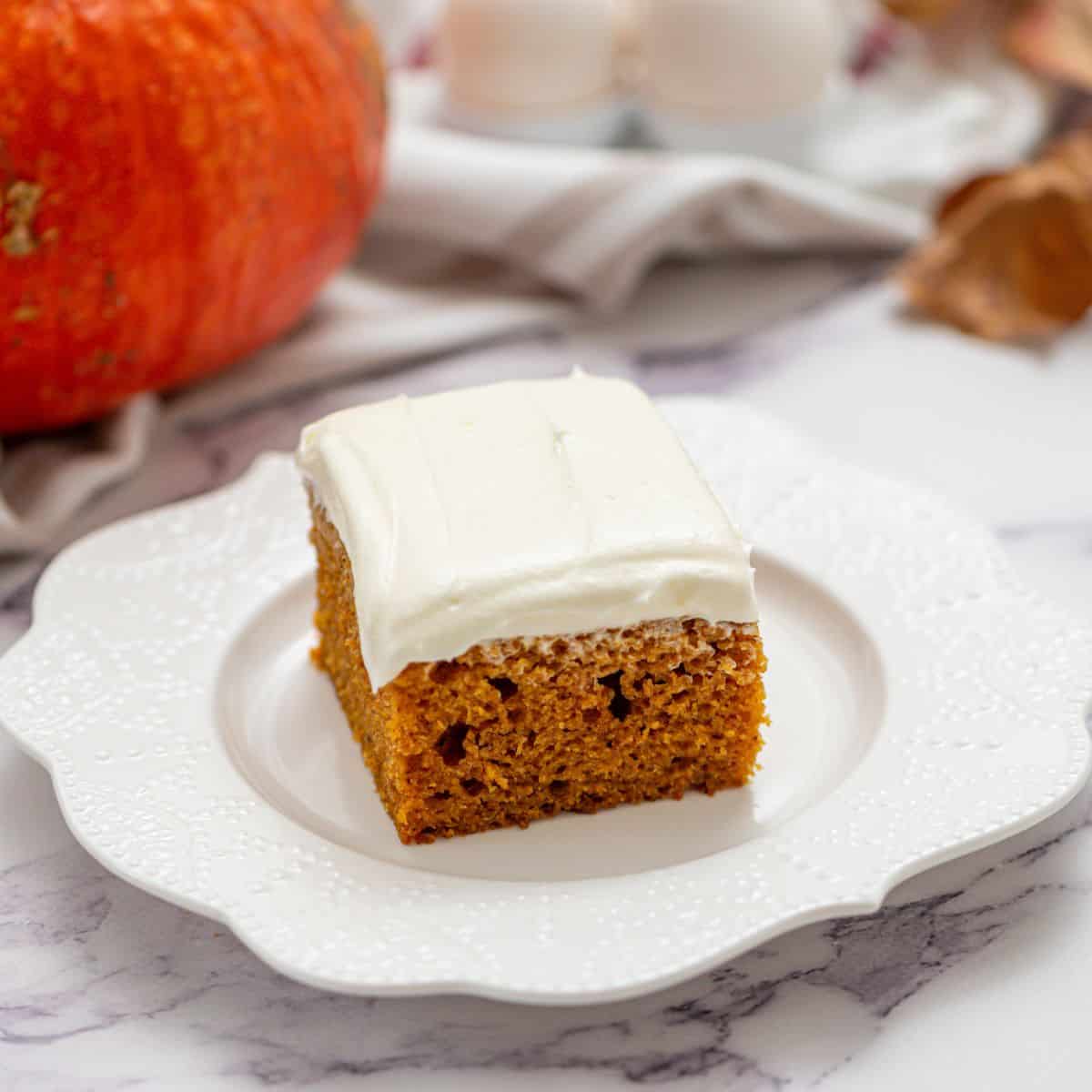 Slice of pumpkin cake with cream cheese frosing on white plate.