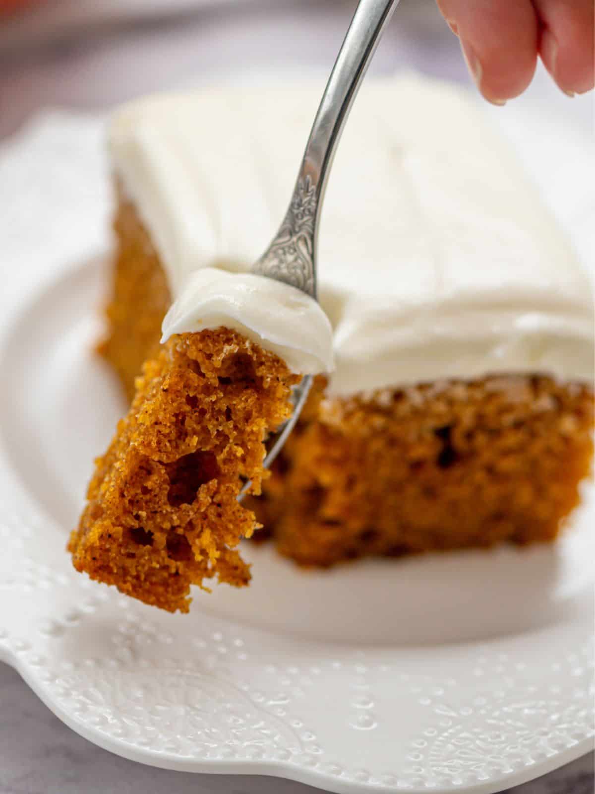 Fork with bite of pumpkin spice cake that is iced with cream cheese frosting.