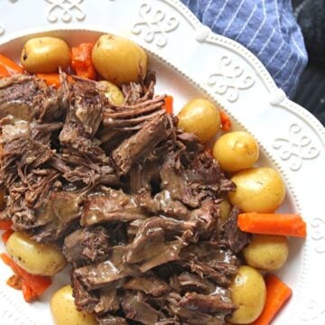 Instant Pot Pot Roast sliced up on white platter with carrots and potatoes.