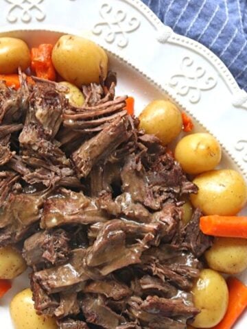 Instant Pot Pot Roast sliced up on white platter with carrots and potatoes.